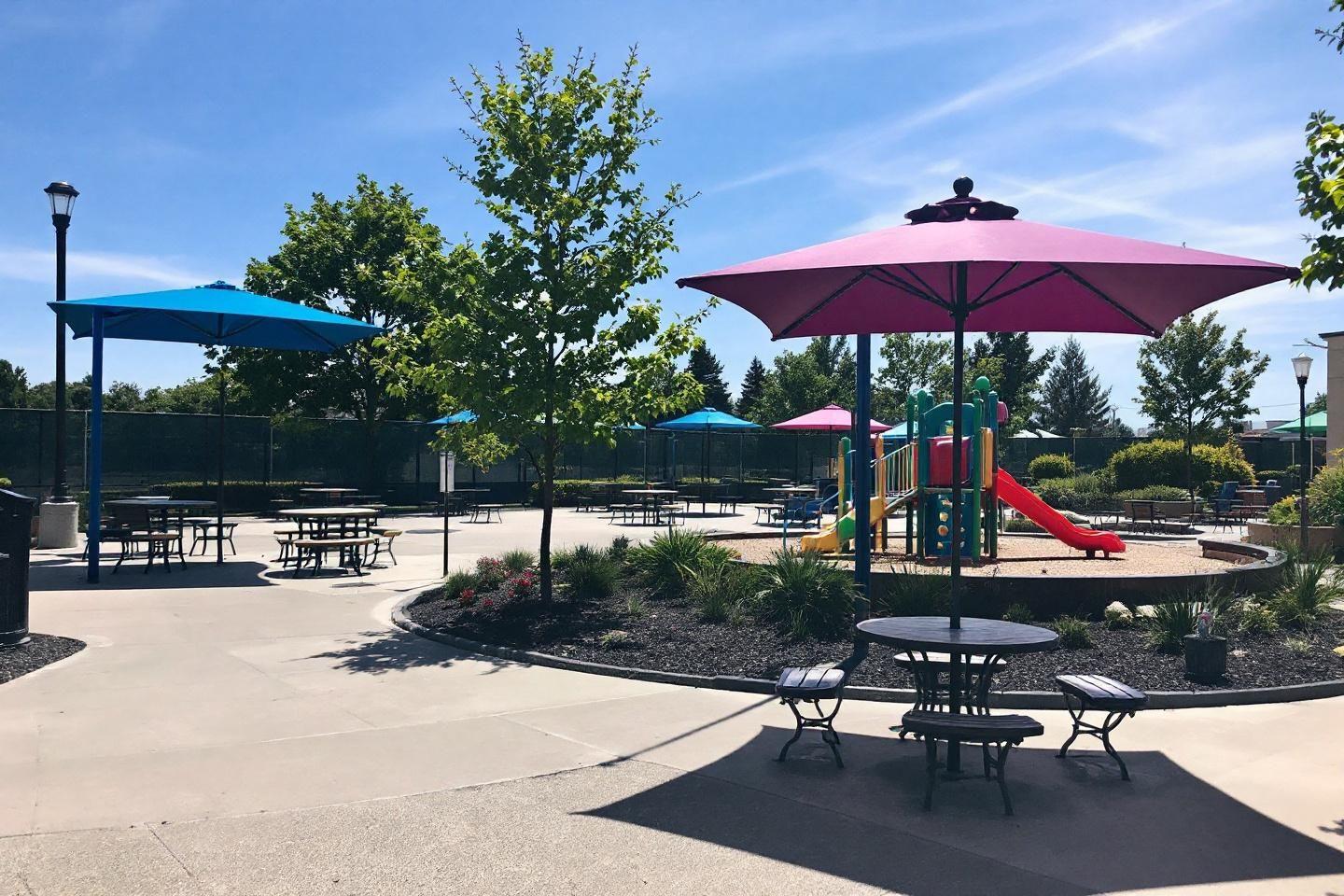 Terrain de jeux avec parasols bleus et roses, tables et toboggan